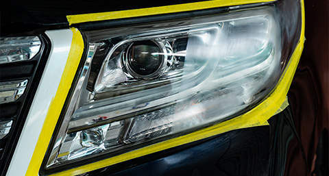 a headlight bordered with yellow tape highlighting the half that has been polished versus the other that is not